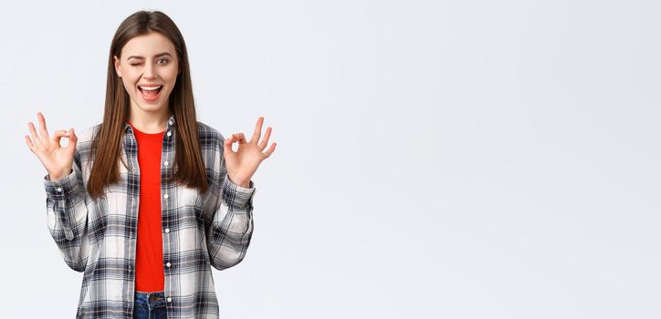 Lifestyle, different emotions, leisure activities concept. Confident and assured enthusiastic young woman in checked shirt assure all okay, promise or guarantee, show okay sign, smiling and wink.