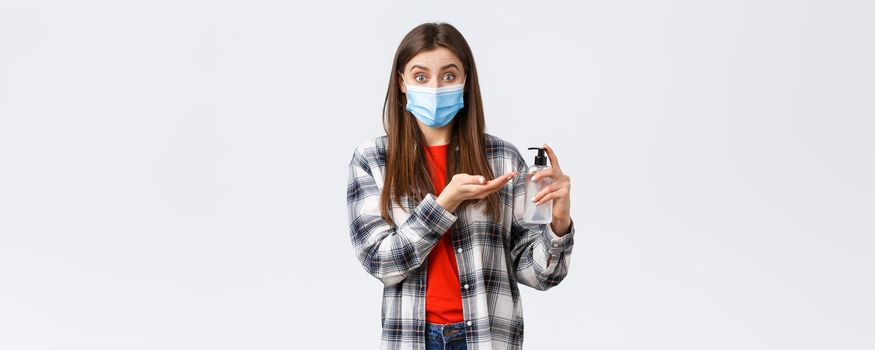 Coronavirus outbreak, leisure on quarantine, social distancing and emotions concept. Smiling girl preventing catching virus, wear medical mask and apply hand sanitizer, white background.