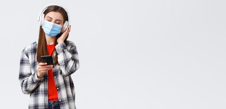 Social distancing, leisure and lifestyle on covid-19 outbreak, coronavirus concept. Carefree and relaxed woman in medical mask, close eyes enjoying music in headphones, hold mobile phone.