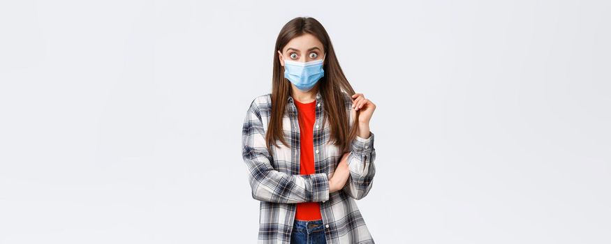 Coronavirus outbreak, leisure on quarantine, social distancing and emotions concept. Shocked and curious young girl in medical mask and checked shirt, stare at friend telling gossip or stunning news.