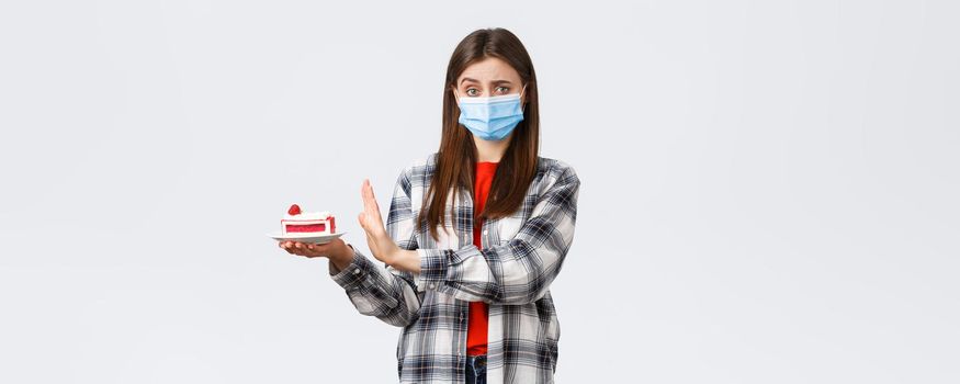 Coronavirus outbreak, lifestyle on social distancing and holidays celebration concept. No thank you. Girl refuse eating this delicious cake as stick to diet, worried over calories, wear medical mask.