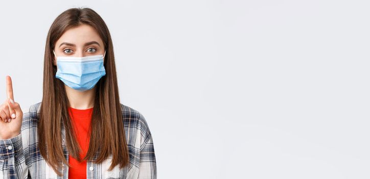 Coronavirus outbreak, leisure on quarantine, social distancing and emotions concept. Close-up of cute young woman in medical mask explain smth, show number one or point up.