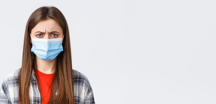 Coronavirus outbreak, leisure on quarantine, social distancing and emotions concept. Close-up of bothered or displeased woman in medical mask, condemn someone, frowning upset.