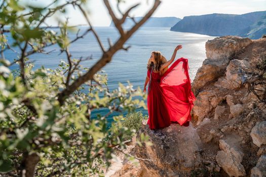 A woman in a flying red dress fluttering in the wind and a straw hat against the backdrop of the sea