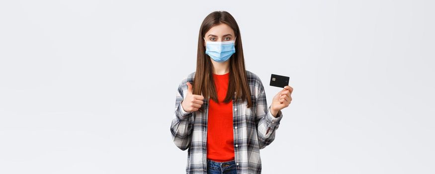 Coronavirus outbreak, working from home, online shopping and contactless payment concept. Satisfied woman in medical mask recommend use credit card during pandemic, thumb-up.