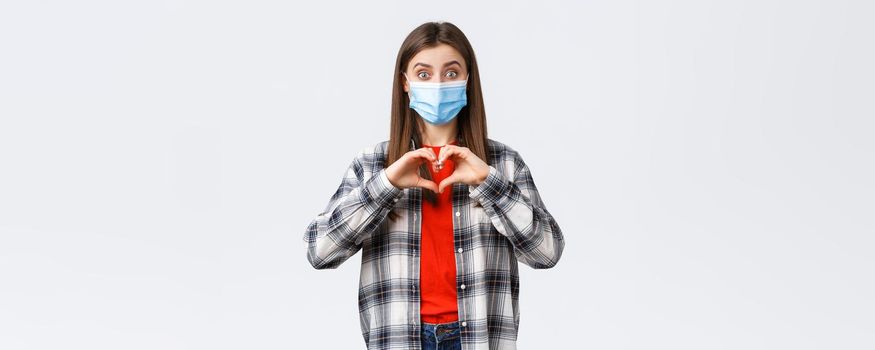 Different emotions, covid-19 pandemic, coronavirus self-quarantine and social distancing concept. Excited young woman in medical mask making confession, show heart sign like someone, express sympathy.
