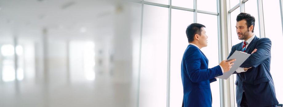 Two business people talk project strategy at office in widen view meeting room. Businessman discuss project planning with colleague at modern workplace .