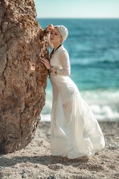 Middle aged woman looks good with blond hair, boho style in white long dress on the beach decorations on her neck and arms