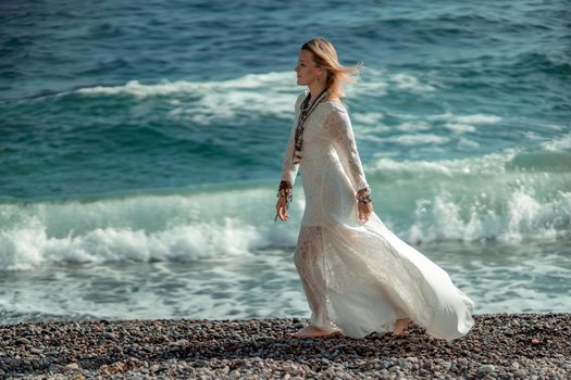 Middle aged woman looks good with blond hair, boho style in white long dress on the beach decorations on her neck and arms