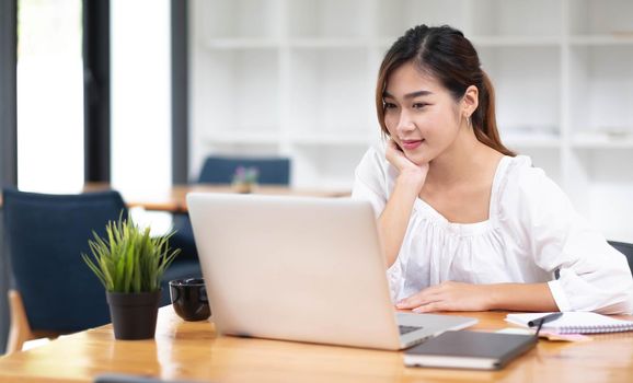 Happy young asian businesswoman sitting on her workplace in the office. Young woman working at laptop in the office..