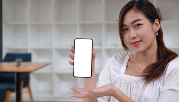 Mockup image of a smiley Asian beautiful woman holding and showing black mobile phone with blank white screen..