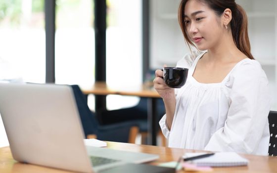 Happy young asian businesswoman sitting on her workplace in the office. Young woman working at laptop in the office..