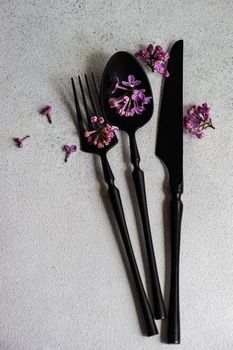 Minimalistic cutlery set with spring lilac flower blossom on concrete background