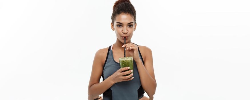 Healthy and Fitness concept - Beautiful American African lady in fitness clothing drinking healthy vegetable drink. Isolated on white background