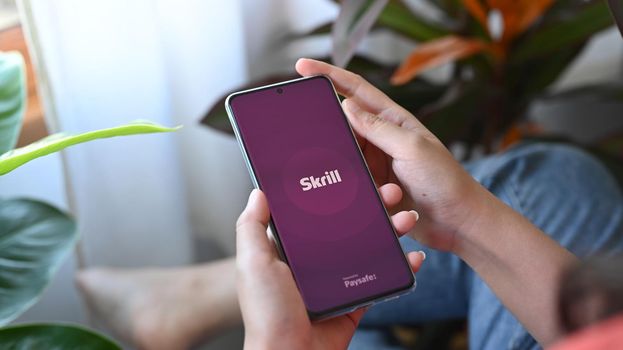 Chiang Mai, Thailand. Jan 30, 2022.Woman holding smart phone with Skrill application on screen. Skrill is an online electronic finance payment system.