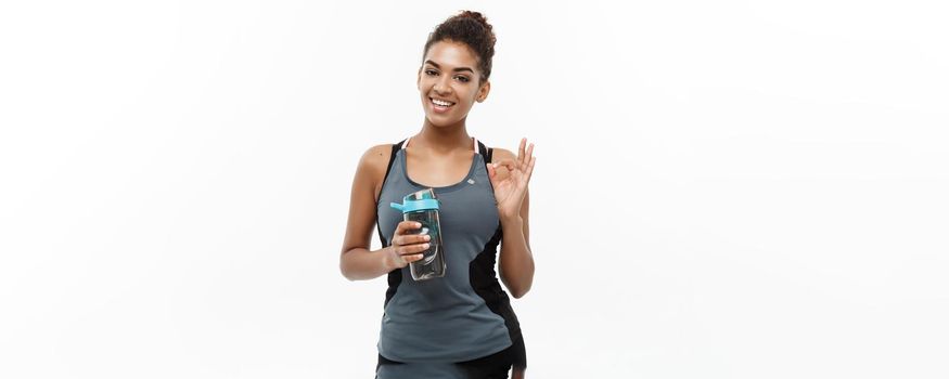 Healthy and Fitness concept - beautiful African American girl in sport clothes holding water bottle after workout. Isolated on white studio background.