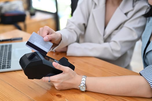 Cropped shot two female customer swiping a credit card through through payment terminal.