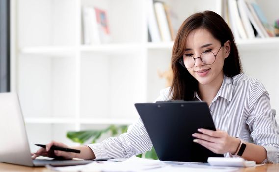 Charming asian businesswoman sitting working on laptop in office..