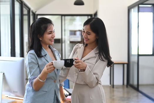 Two business women discussing project or sharing news during coffee break in office.