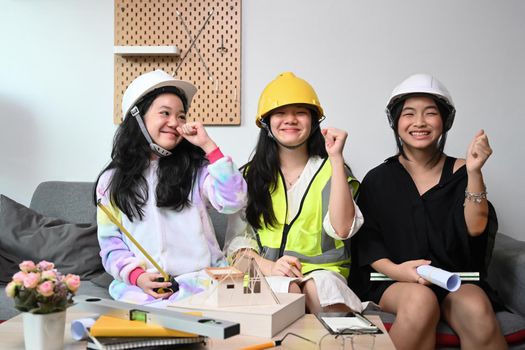 Three lovely asian kids in safety helmet pretend to be engineer playing together at home.