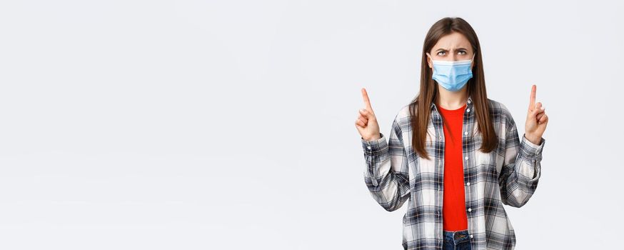 Coronavirus outbreak, leisure on quarantine, social distancing and emotions concept. Confused and doubtful young woman looking and pointing up with suspicious, disbelief face.