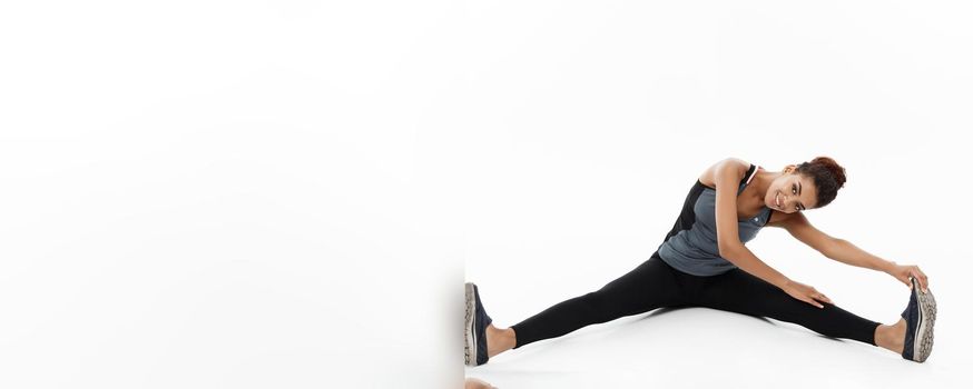 Sport, training, lifestyle and Fitness concept - portrait of beautiful happy African American woman stretching leg while sitting. Isolated on white studio background