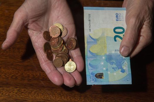 Wrinkled hands of elderly woman holding coins and euro banknote. Close up.