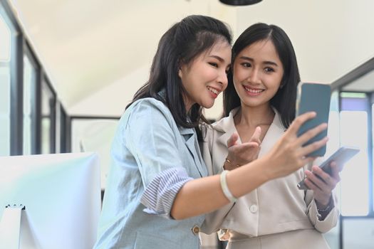 Two female business colleagues taking a selfie with smart phone at workplace.