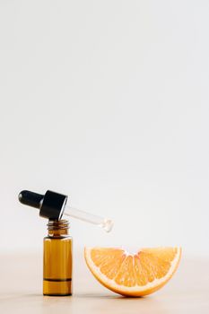 Essential oil in one bottle and a piece of orange standing on the surface.