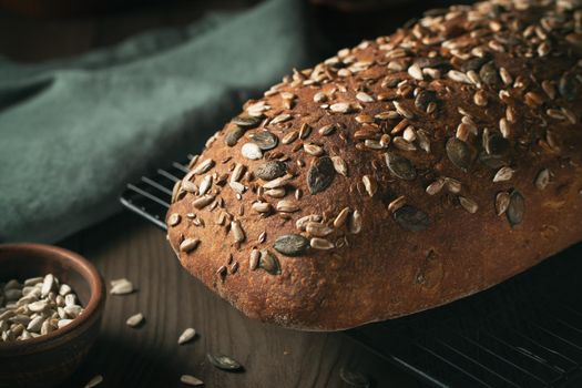 Loaf of homemade whole grain bread with seeds cool down on a wire rack on a wooden table.