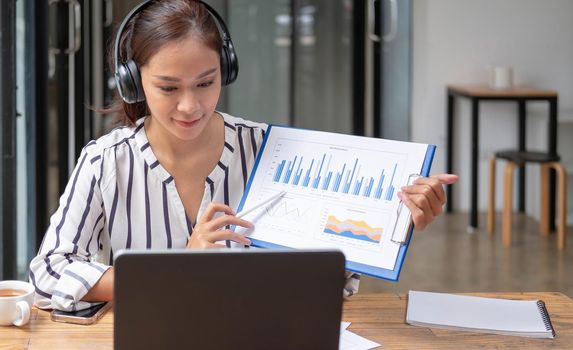 Happy asian woman young wearing headset, communicating with client via video computer call..