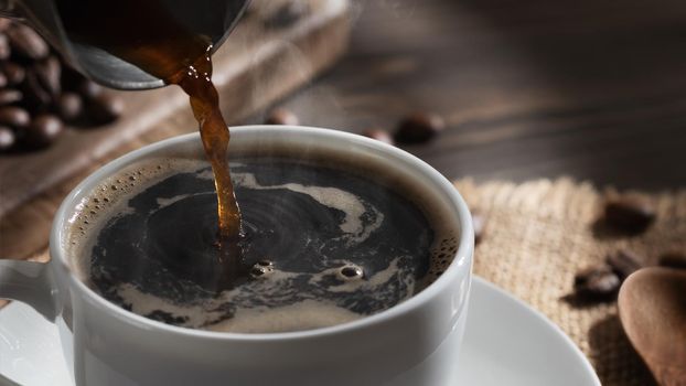 Pouring freshly brewed hot cezve coffee into a white cup, close up.