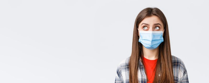 Coronavirus outbreak, leisure on quarantine, social distancing and emotions concept. Close-up of thoughtful, young woman in medical mask, look upper left corner reading sign or have bubble thought.