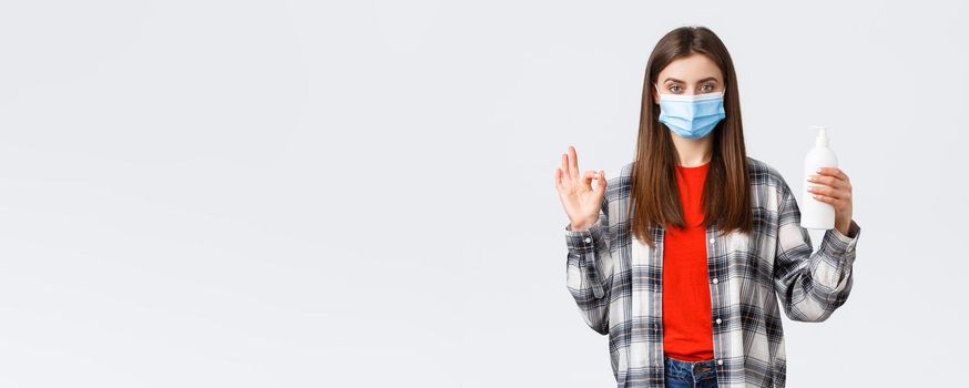 Coronavirus outbreak, leisure on quarantine, social distancing and emotions concept. Self-assured young woman in medical mask recommend hand soap or sanitizer, show okay sign.