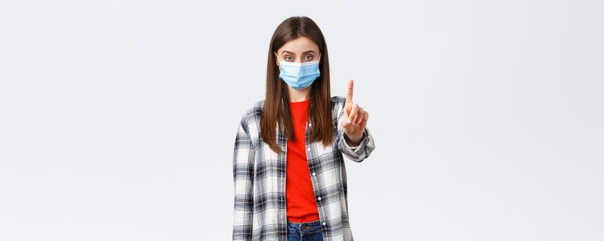 Coronavirus outbreak, leisure on quarantine, social distancing and emotions concept. Serious young woman, elder sister in medical mask shaking finger in stop, prohibition, stay home.