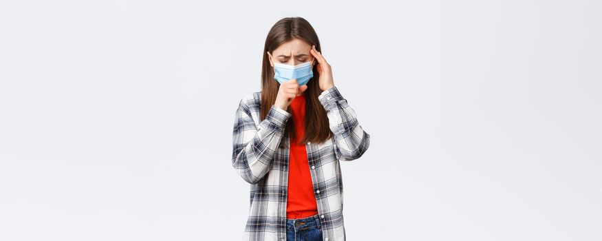 Coronavirus outbreak, leisure on quarantine, social distancing and emotions concept. Young woman feel sick, wear medical mask and coughing, touch temple as headache, high fever.