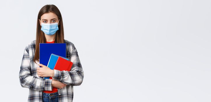 Coronavirus pandemic, covid-19 education, and back to school concept. Young female student in medical mask holding notebooks, going to class, freshman in university in personal protective facemask.