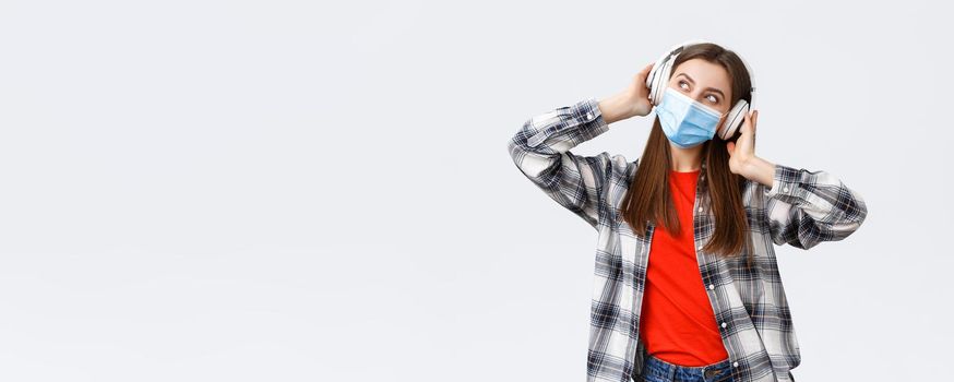 Social distancing, leisure and lifestyle on covid-19 outbreak, coronavirus concept. Happy carefree attractive girl in medical mask, look away dreamy, imaging while listening music in headphones.