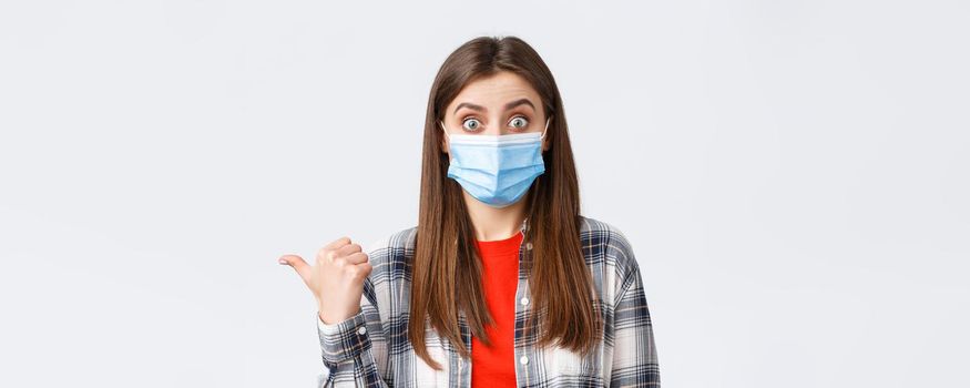 Coronavirus outbreak, leisure on quarantine, social distancing and emotions concept. Astonished and impressed cute woman in medical mask showing way, talking about banner on left side.