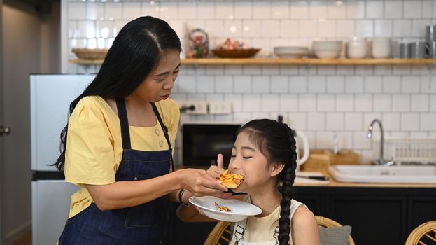 Asian mom and her little sweet daughter spending time together in home kitchen. Family, children, love and happy people concept.