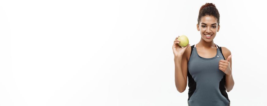 Healthy and Fitness concept - Beautiful American African lady in grey fitness clothes holding green apple. Isolated on white background