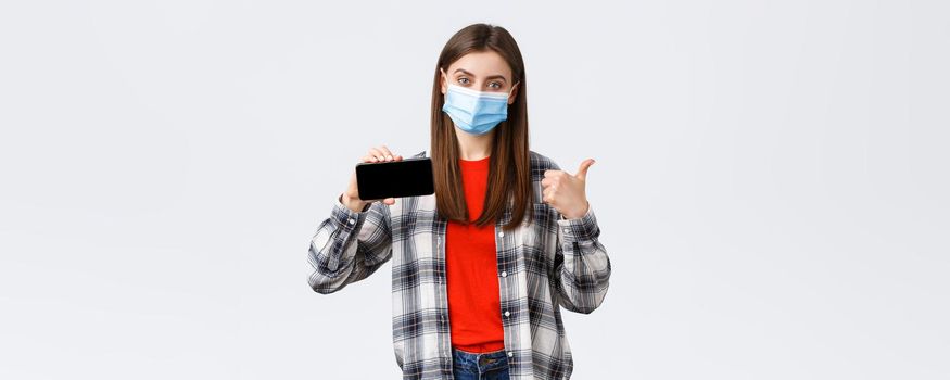 Different emotions, covid-19, social distancing and technology concept. Satisfied smiling girl in medical mask, show thumb-up and mobile phone screen, recommend application or link.