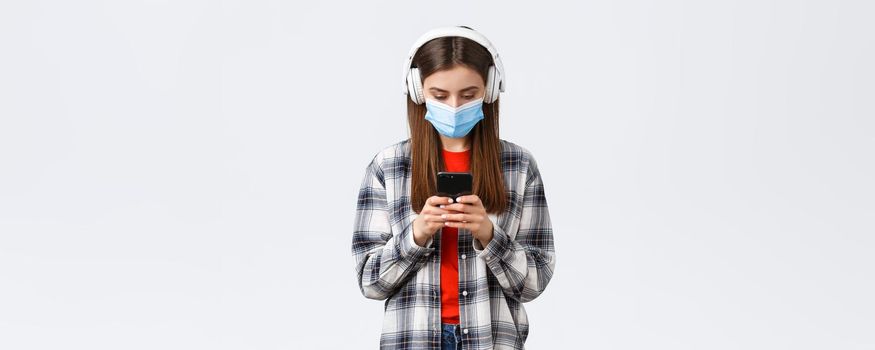 Social distancing, leisure and lifestyle on covid-19 outbreak, coronavirus concept. Cute female student, teenage girl in headphones picking song in mobile phone, download music app, white background.