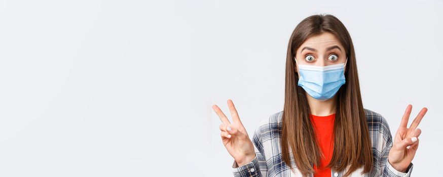 Coronavirus outbreak, leisure on quarantine, social distancing and emotions concept. Close-up of excited and thrilled cute woman in medical mask, showing peace sign or quotes, stare impressed.