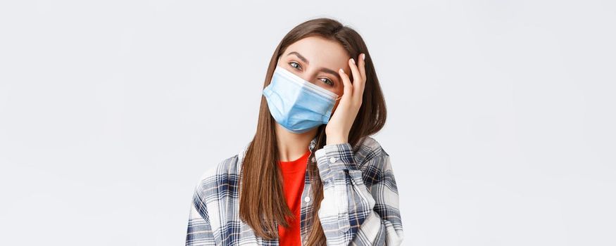 Coronavirus outbreak, leisure on quarantine, social distancing and emotions concept. Close-up of tender happy young woman in medical mask, tilt head, flirting and playing with hair.