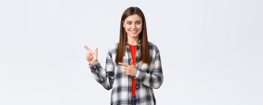 Lifestyle, different emotions, leisure activities concept. Pleasant smiling brunette girl in checked shirt, pointing fingers left, showing way to promo, recommend click link or buy product.