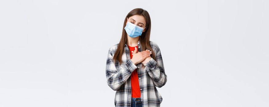 Coronavirus outbreak, leisure on quarantine, social distancing and emotions concept. Dreamy attractive young woman in medical mask, close eyes imaging or remember memory, press hands to heart.