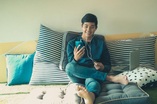 asian male teenager man listening to music from smart mobile phone while sitting on floor at home