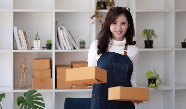 Startup SME small business entrepreneur SME or freelance Asian woman using a laptop with box, Young success Asian woman with her hand lift up, online marketing packaging box and delivery, SME concept..