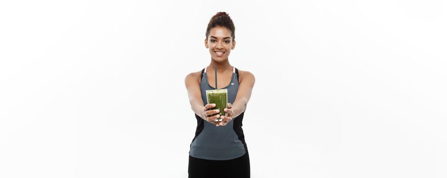 Healthy and Fitness concept - Beautiful American African lady in fitness clothing drinking healthy vegetable drink. Isolated on white background